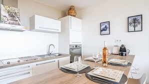 Ett modernt kök med vita skåp, en diskho i rostfritt stål och ett matbord i trä med plats för fyra personer.