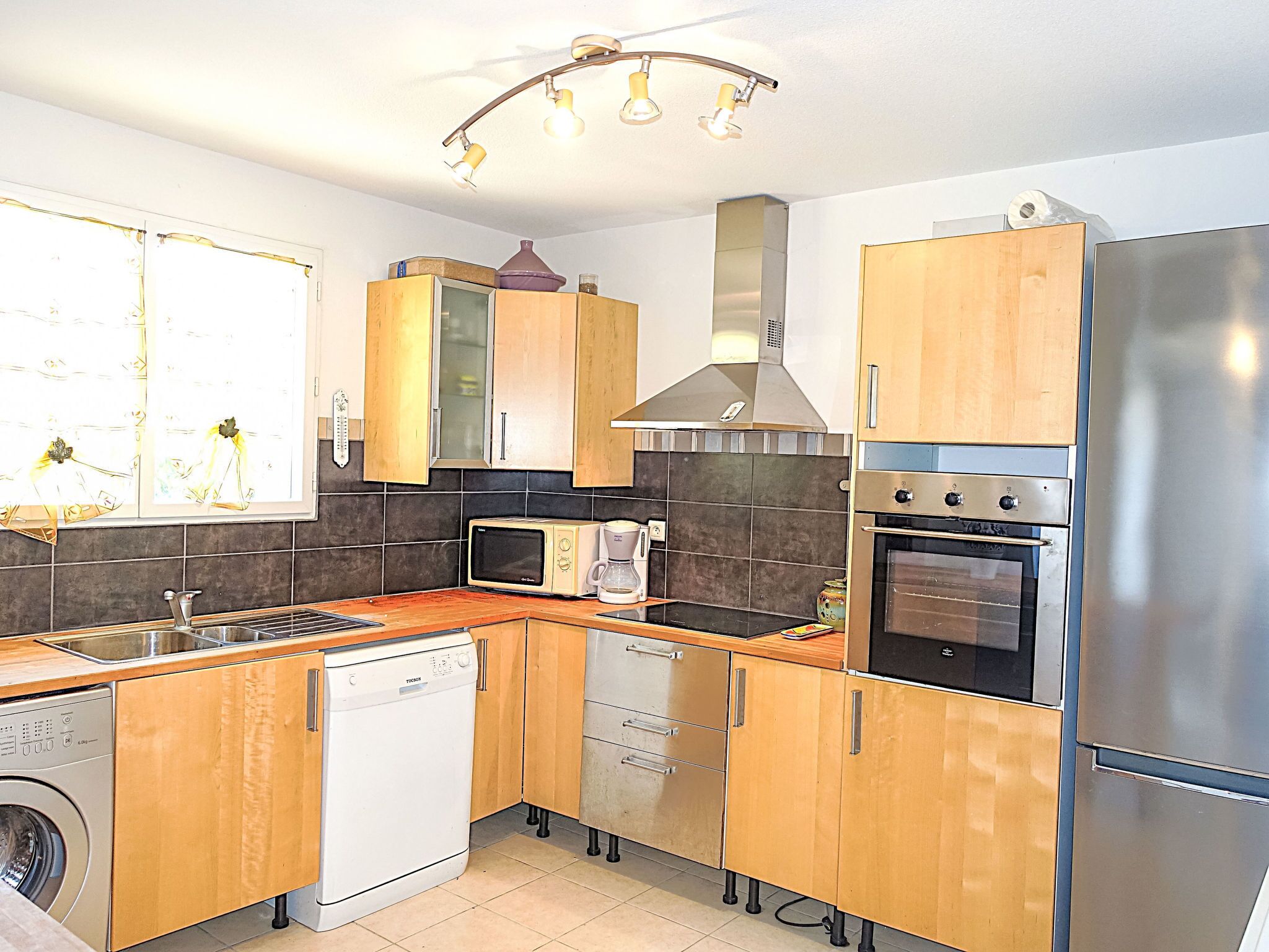 A compact kitchen with wooden cabinets, a stainless steel refrigerator, a microwave, a dishwasher, and a stove.