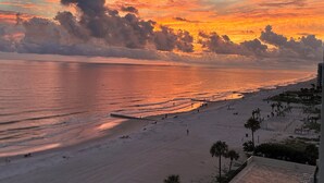 Ein Strand bei Sonnenuntergang, mit einer Promenade und Palmen.