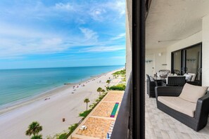 Un balcon donnant sur une plage, des meubles en osier et un sol carrelé.
