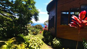 A wooden house with a curved roof, surrounded by lush greenery and a garden with various plants and flowers.