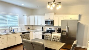 A modern kitchen with white cabinets, a stainless steel refrigerator, a dining table with chairs, and a built-in oven. - American Pharoah Cottage | 3BR Downtown Versailles (Versailles)