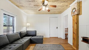Una sala moderna con un sofá modular, un ventilador de techo, piso de madera y una puerta que da a otra habitación.