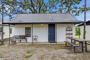 A small, single-story building with a blue door, a bench, and a table outside. - Tenkiller Maple Cabin Escape Near Lake Adventures F (Cookson)
