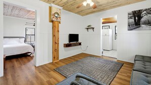 Un dormitorio con cama, televisor, un revestimiento de madera en la pared y ventilador de techo.