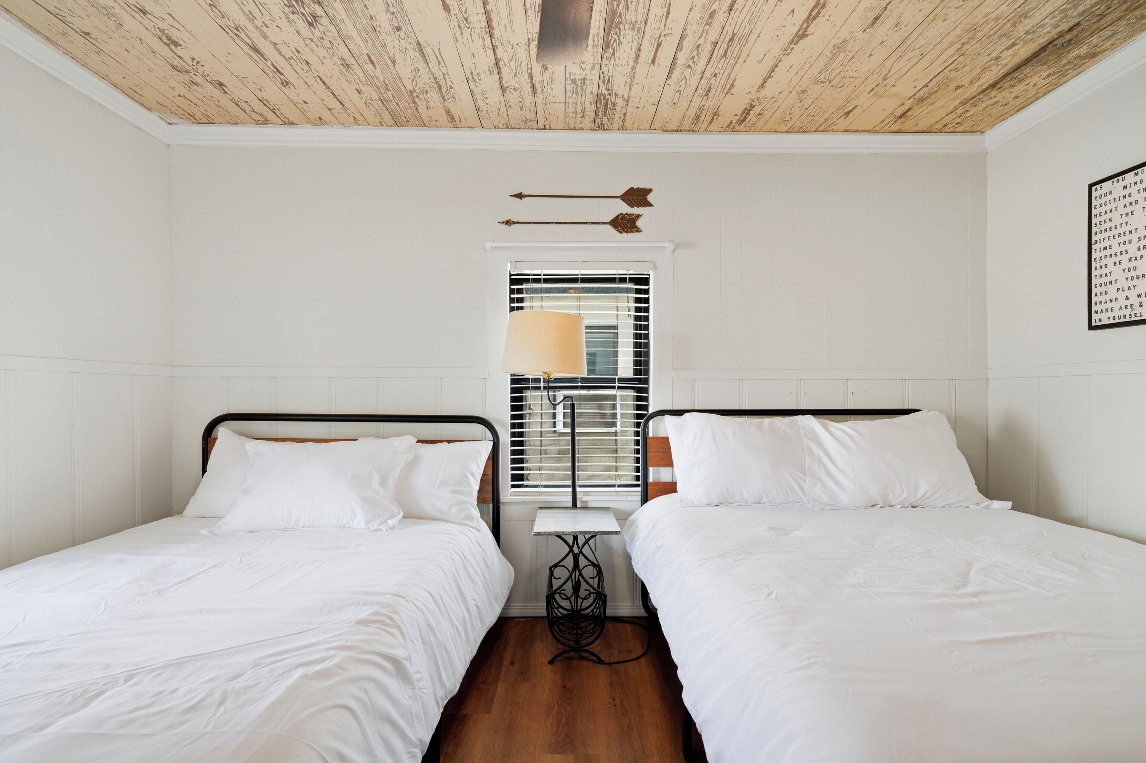 A room with two single beds, a small table, and a window with blinds.