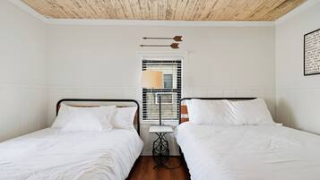 A room with two single beds, a small table, and a window with blinds.
