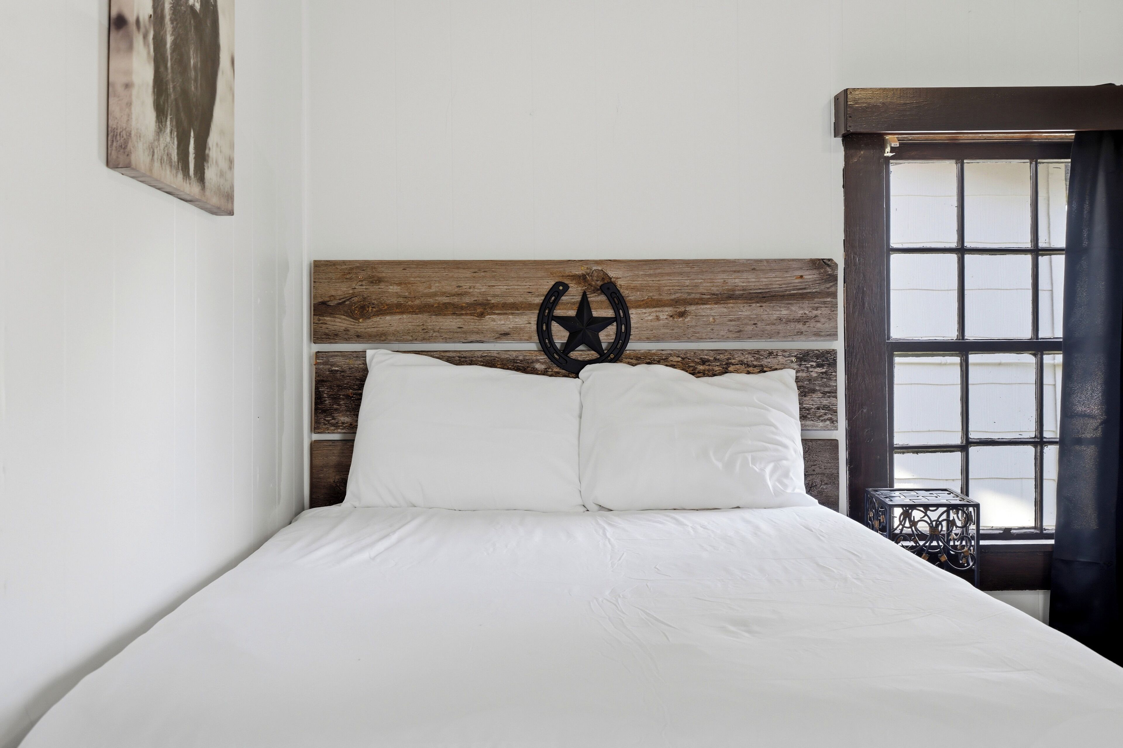 Una cama con cabecera de madera, ropa de cama blanca y un adorno metálico.