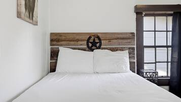 Una cama con cabecera de madera, ropa de cama blanca y un adorno metálico.