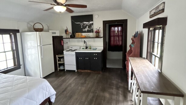 A compact kitchen with a refrigerator, stove, and sink. There is a bed and a wooden bench with stools. - Tenkiller Cedar Cabin Escape Near Lake Adventures B (Cookson)