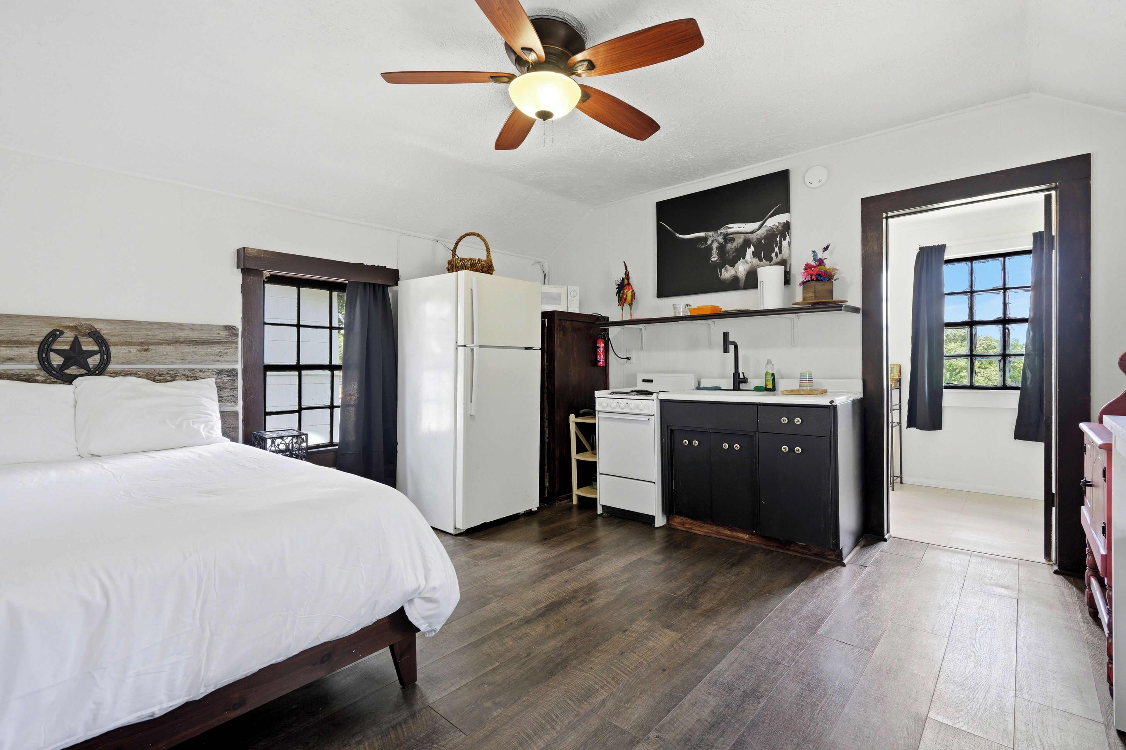 A bedroom with a bed, a white refrigerator, a stove, and a ceiling fan.