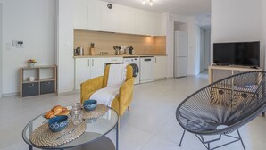 A modern living room with a glass coffee table, a yellow armchair, a black wire chair, and a TV on a wooden stand. - 151 Bay Street by Interhome (Cavalaire)