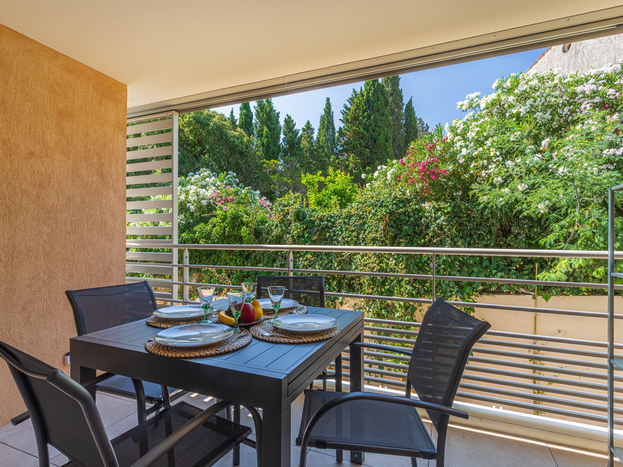 A balcony with a table set for four, overlooking a garden with various plants and flowers.