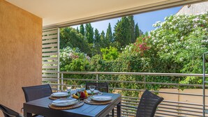 A balcony with a table set for four, overlooking a garden with various plants and flowers. - 151 Bay Street by Interhome (Cavalaire)