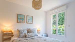 A bedroom with a large bed, two bedside lamps, a window with a view of greenery, and two framed pictures on the wall. - 151 Bay Street by Interhome (Cavalaire)