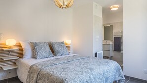 Et soveværelse med en stor seng, sengeborde med lamper, en hængende lampe og udsigt til badeværelset.