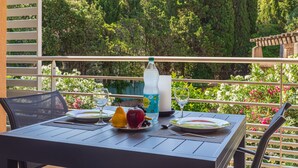 En balkon med et bord dækket til to personer, med en vandflaske, en tallerken med frugt og et glas.