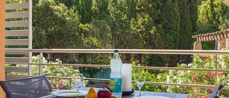 A balcony with a table set for two, featuring a bottle of water, a plate with fruit, and a glass.