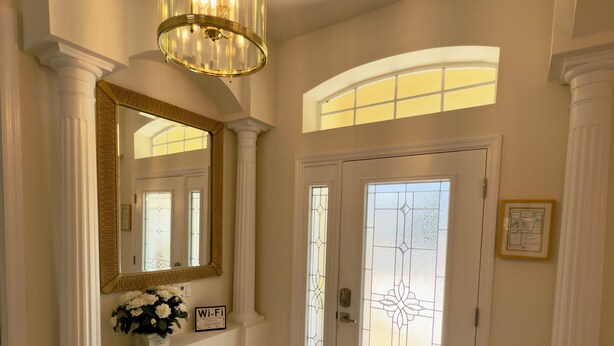 A hallway with a chandelier, a double door with stained glass, and a mirror above a flower arrangement. - Resort Villa! Pool, Hot Tub & Game Room by Disney! (Kissimmee)