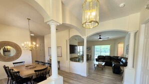A spacious living area with a dining table, black leather sofa, and a chandelier. - Resort Villa! Pool, Hot Tub & Game Room by Disney! (Kissimmee)