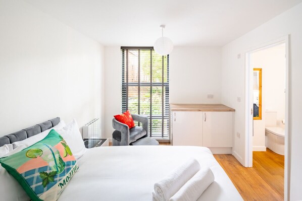 Une chambre à coucher moderne, avec un lit, une chaise, une petite table et une vue sur l’extérieur par une fenêtre.