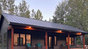 A modern log cabin with a covered porch, outdoor seating, and a gravel pathway leading to the entrance.