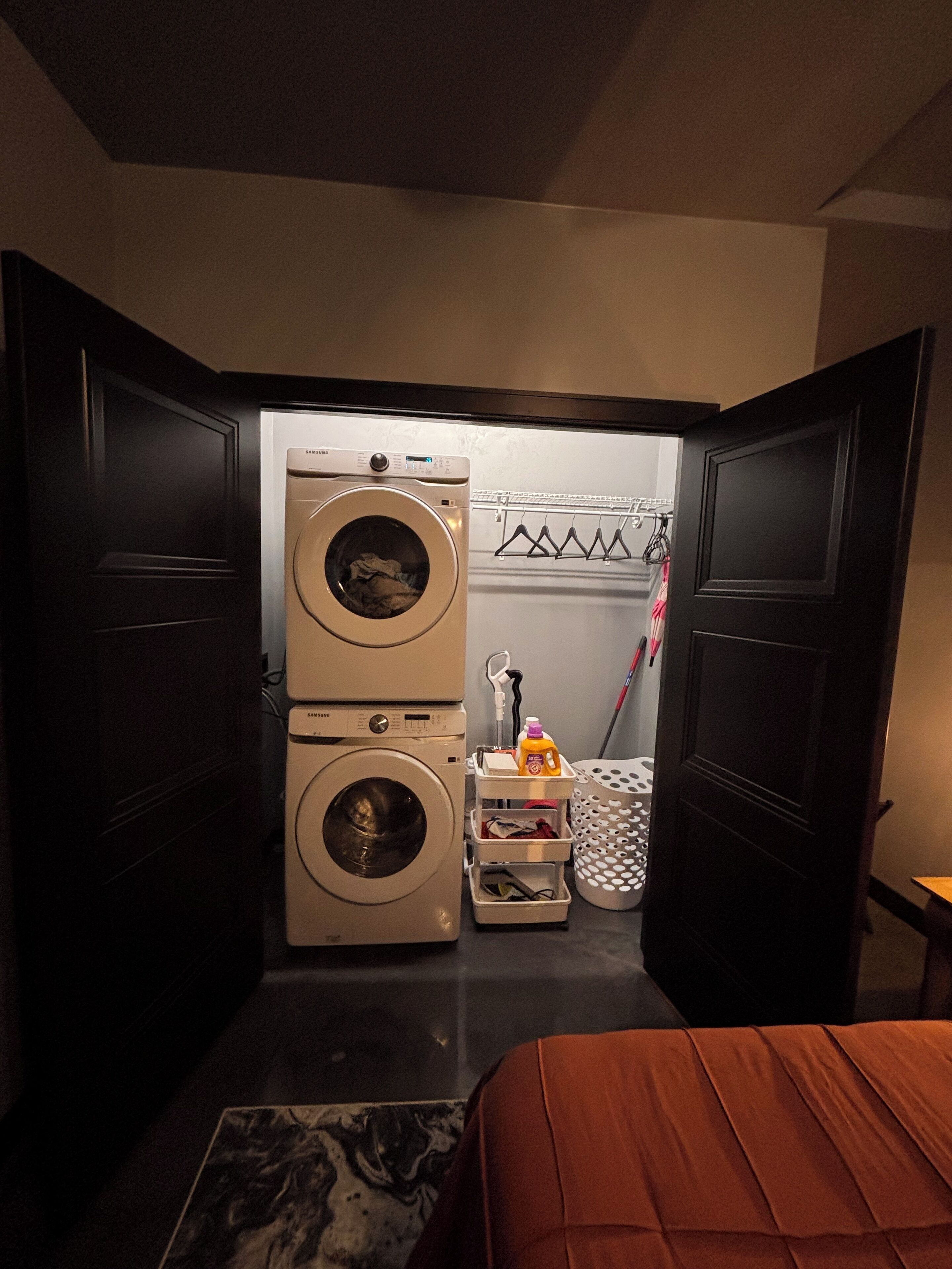 Habitación pequeña con lavadora, tendedero y cama.