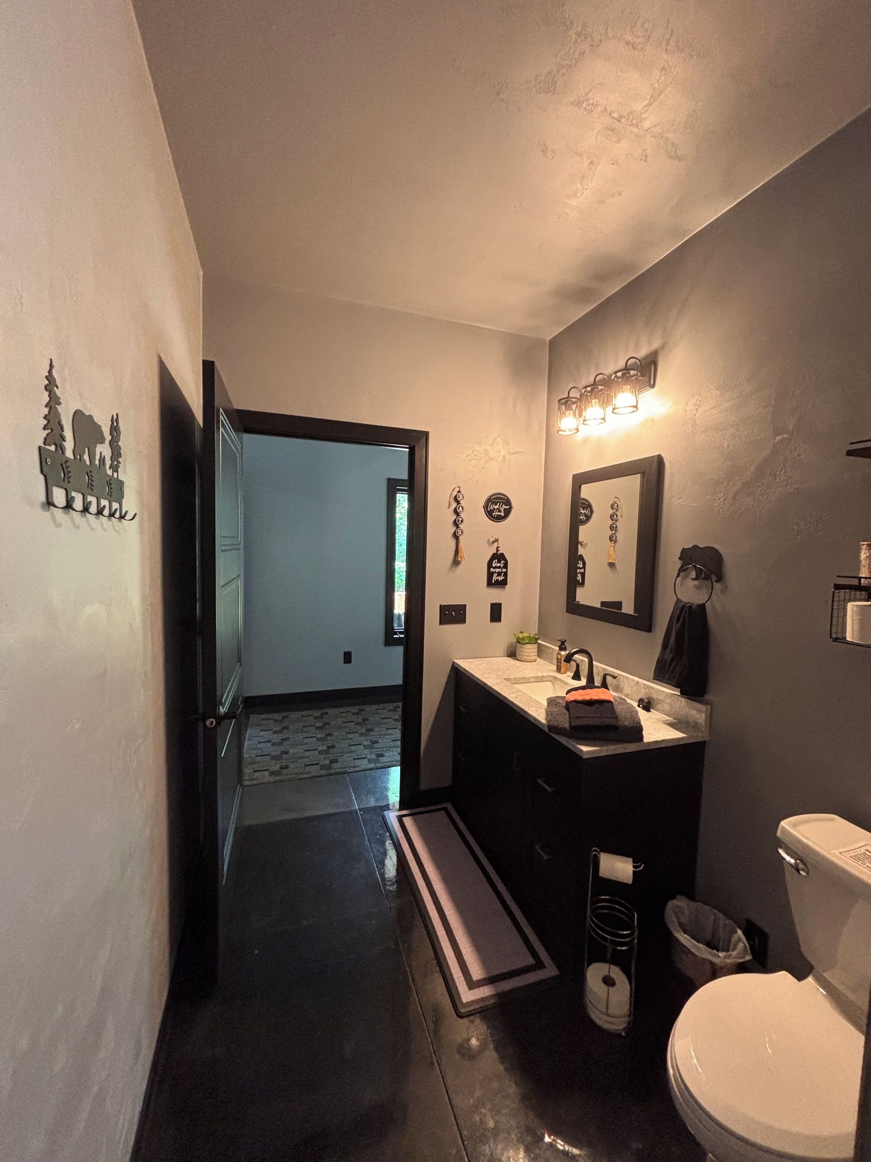 A modern bathroom with a dark floor, a white toilet, a sink with a mirror above it, and a small window.