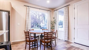 Un comedor con una mesa y sillas de madera, una cocina con refrigerador de acero inoxidable, y vista por la ventana.