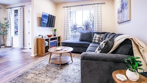 Una sala de estar moderna con un sofá gris, una mesa redonda de centro y un ventanal con cortinas.