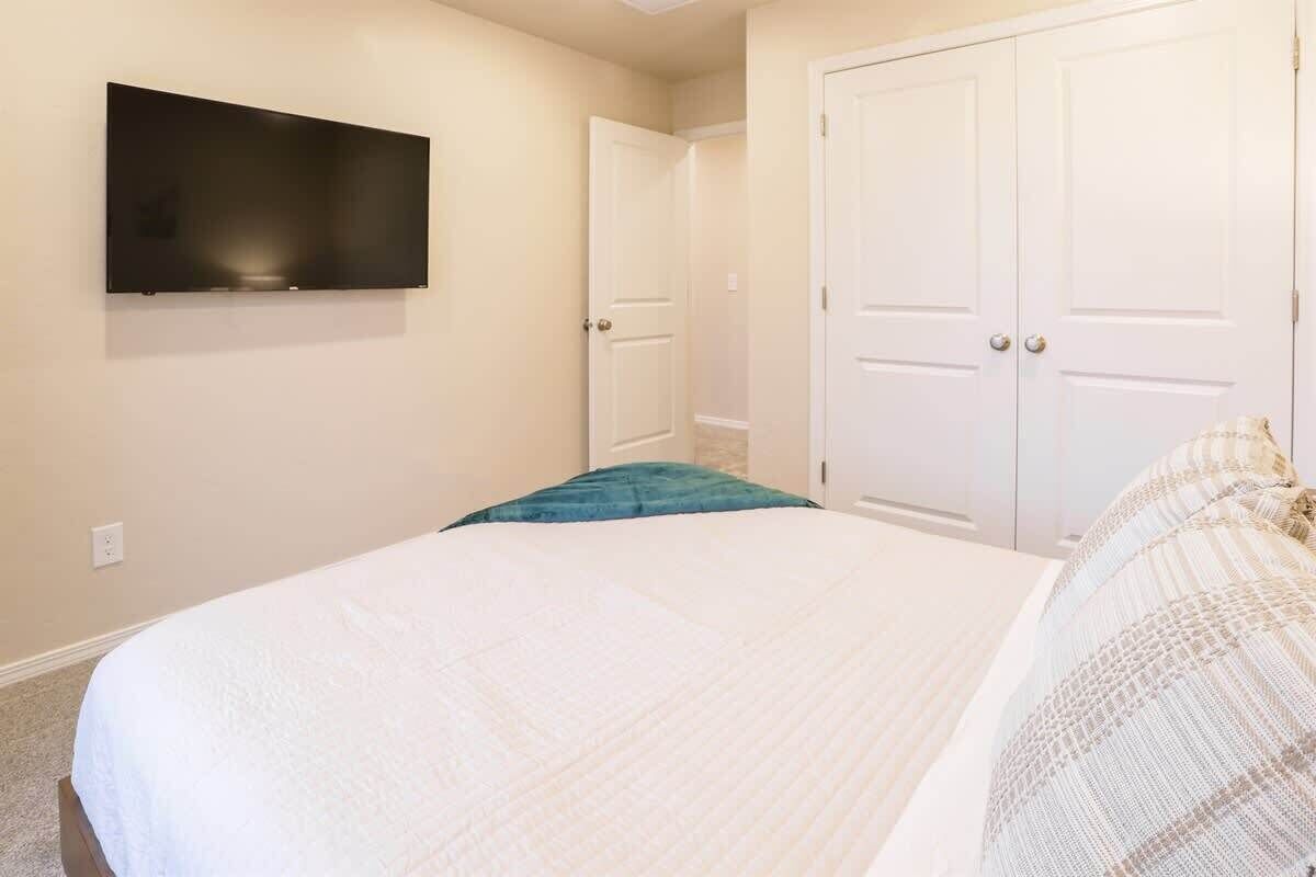 A bedroom with a bed, a flat-screen TV mounted on the wall, and a closet with two doors.
