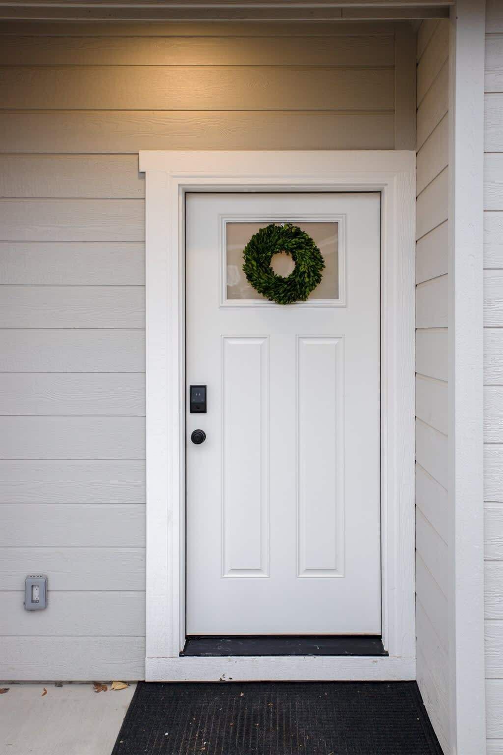 A white front door with a green wreath, a doorbell, and a small window above the door.