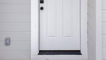 A white front door with a green wreath, a doorbell, and a small window above the door.