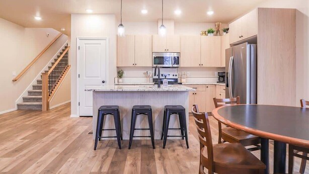 Una cocina moderna con armarios de madera, una isla central con taburetes, una mesa de comedor y una escalera.