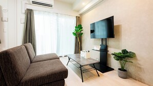 A modern living room with a sofa, a coffee table, a TV mounted on the wall, and a potted plant. - Hotel Reference Ropponmatsu Condominium (Fukuoka)