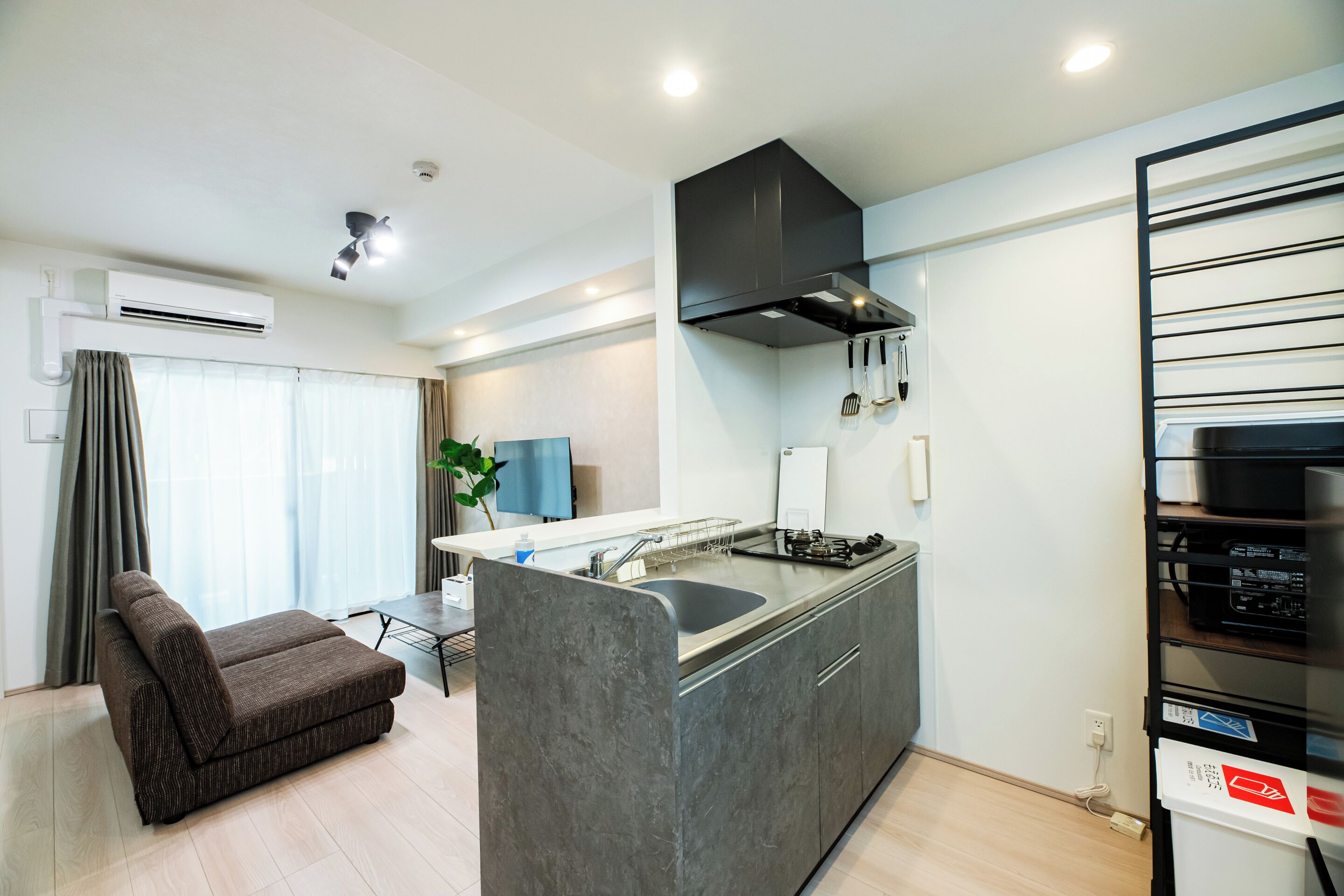 A modern kitchen with a built-in island, a grey sofa, and a dining area with a table and chairs.