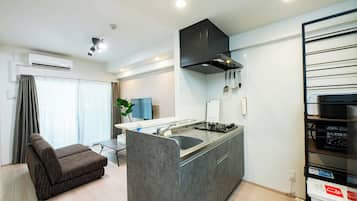 A modern kitchen with a built-in island, a grey sofa, and a dining area with a table and chairs.