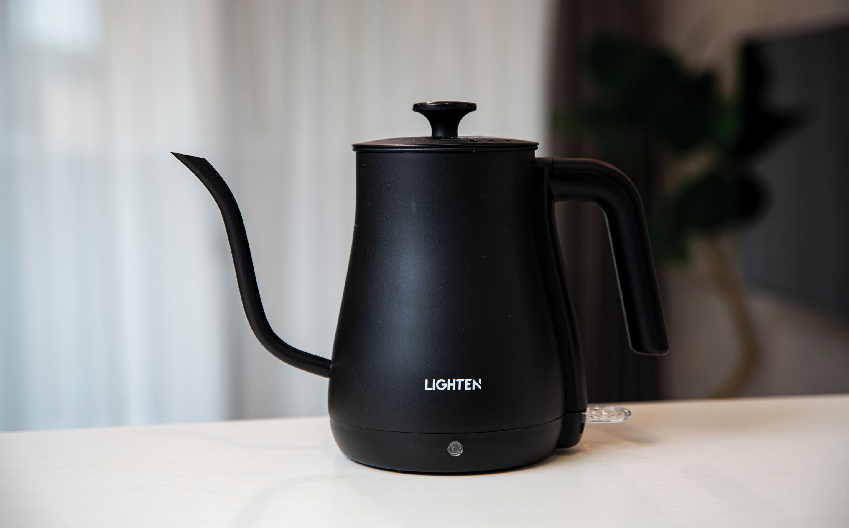 A black electric kettle with a handle and spout, labeled "LIGHTEN," on a white surface.