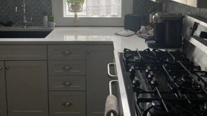 Una cocina con estufa, armarios, una ventana con cortinas y una planta colgante.