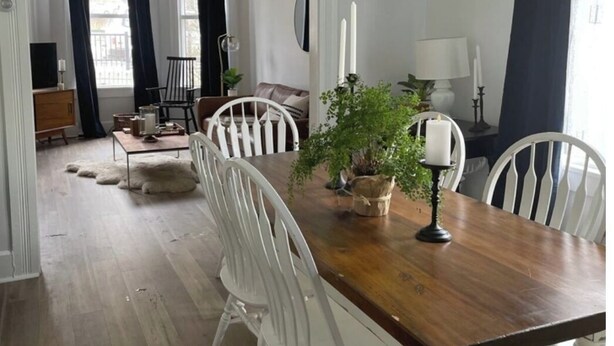 Un comedor con una mesa de madera, sillas blancas, una araña y una planta en maceta.