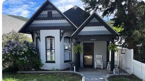 Una casa de dos pisos con fachada blanca y detalles oscuros, un porche con un banco y un buzón.