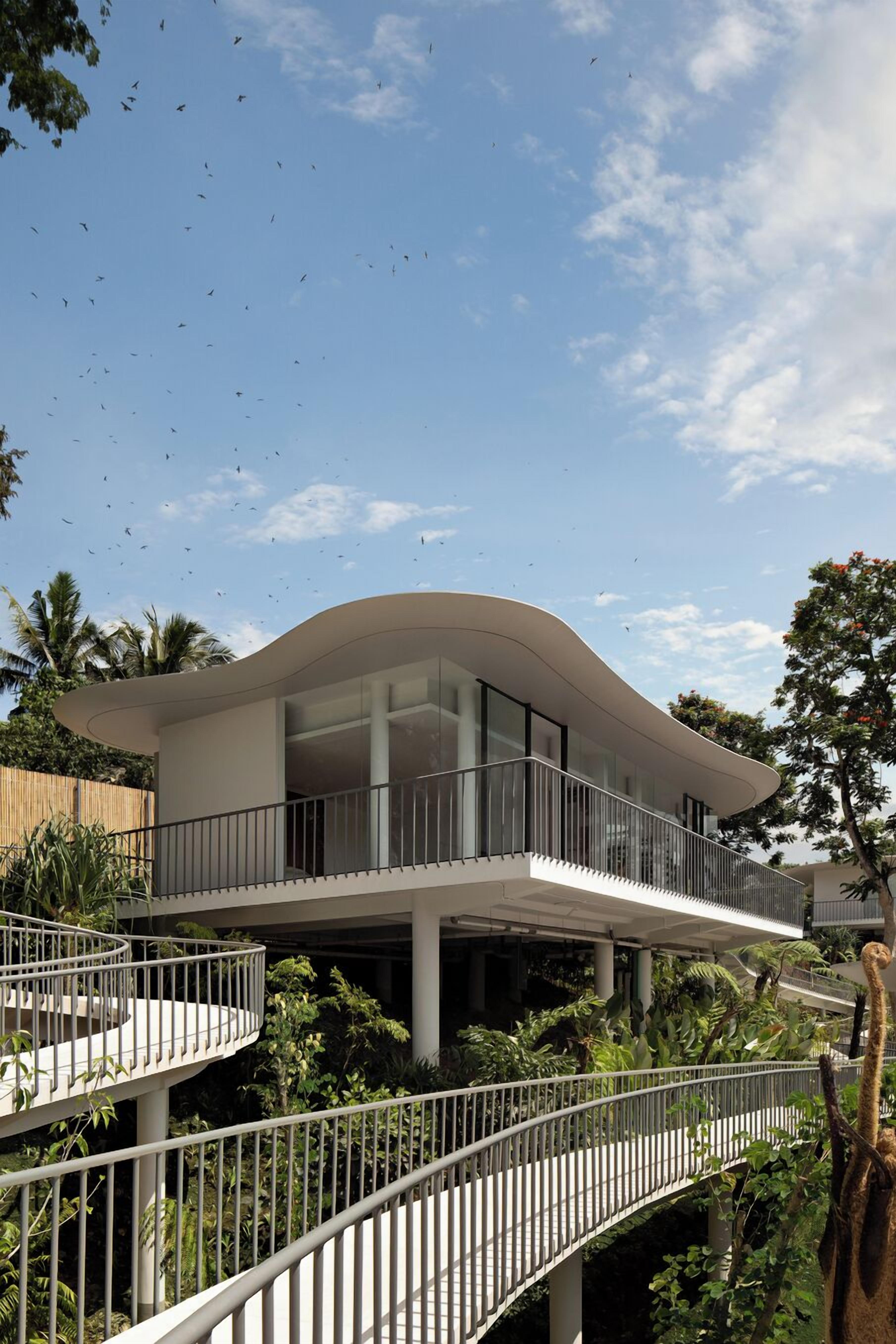 Un edificio moderno con techo curvo, balcón y jardín circundante.