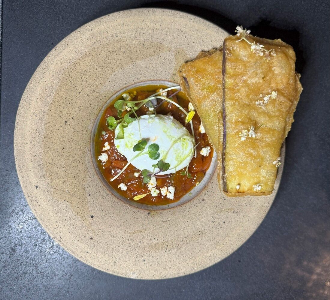 A dish with a poached egg, greens, and crumbled cheese on a plate, accompanied by a piece of bread.