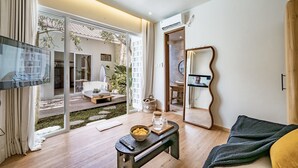A modern living room with a large TV, a bench with a bowl and a glass, and a view of a garden through glass doors.