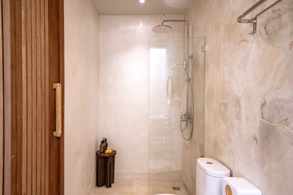 A modern bathroom with a glass shower enclosure, a wooden door, and a small wooden stool with toiletries.