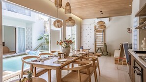 A modern dining area with a wooden table, wicker pendant lights, and a view of a swimming pool.