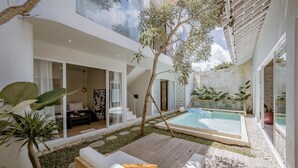 A modern outdoor living area with a pool, wooden deck, and lush greenery.