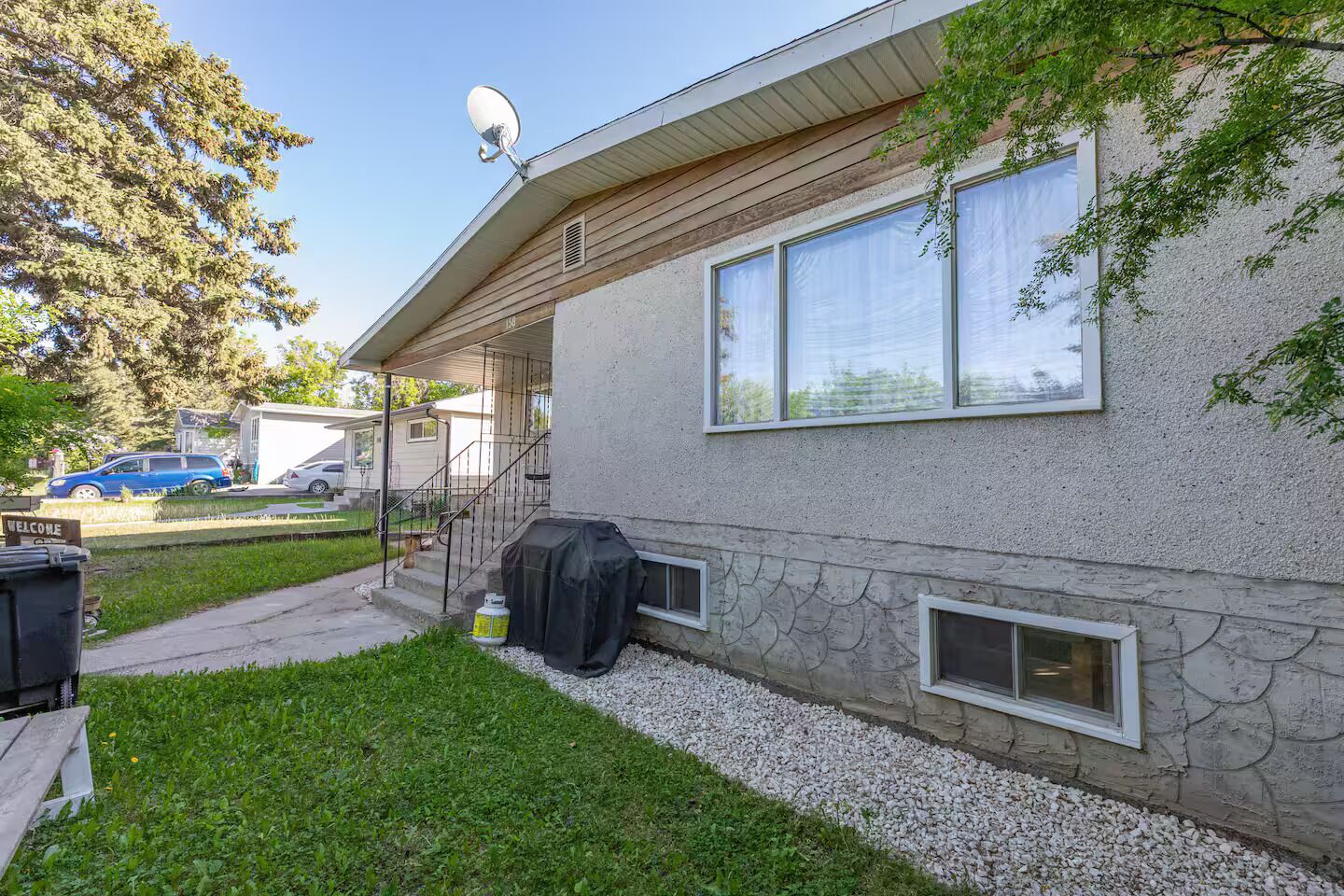 A single-story mobile home with a satellite dish, a covered grill, and a gravel driveway.