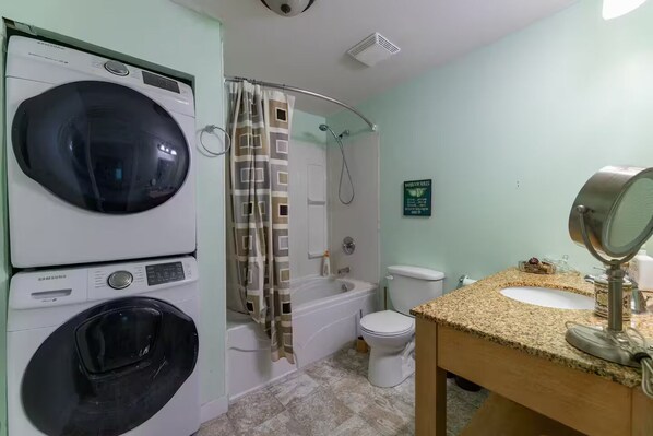 A bathroom with a washing machine, a shower, a toilet, and a sink with a mirror.