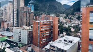 A cityscape with high-rise buildings, a prominent tower with a unique design, and a mountainous backdrop.